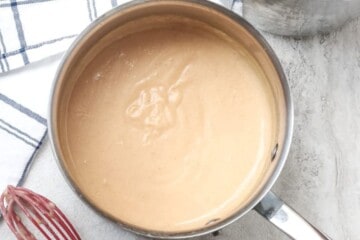 Creamy homemade cream of chicken soup in saucepan next to red whisk.