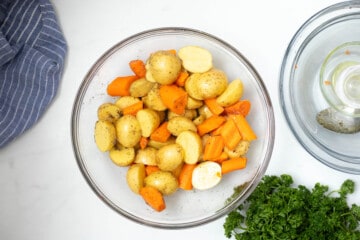 Mixing bowl with halved potatoes and carrots tossed with oil and salt and pepper.