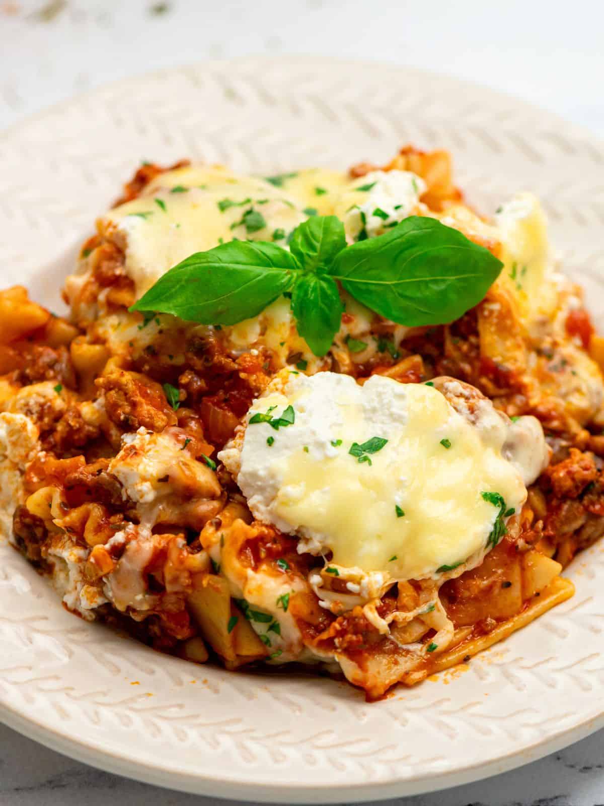 Skillet lasagna served on white plate topped with fresh basil.