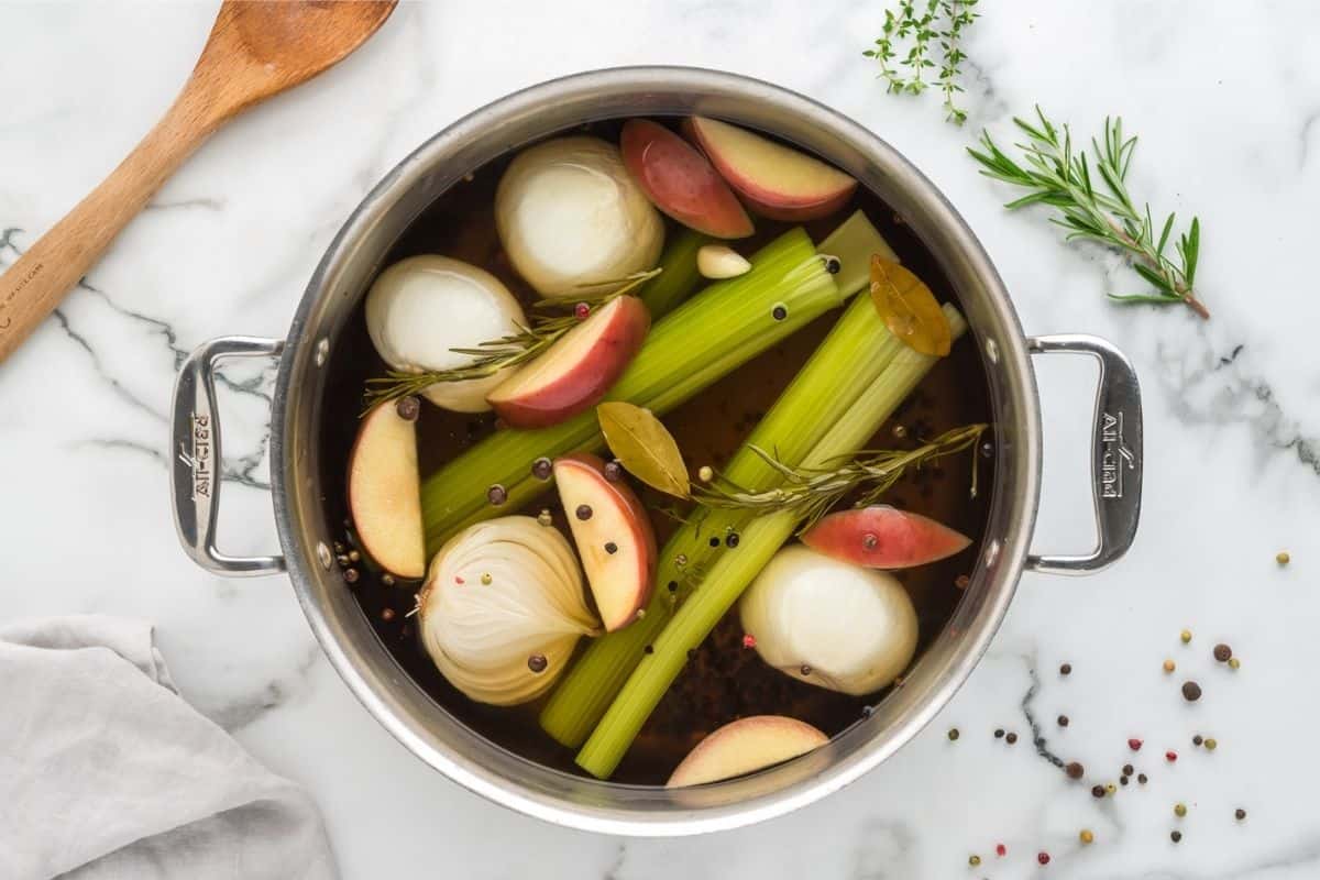 Cooked Turkey brine in large stock pan with apples, onions, peppercorns, onions, and celery in stock pan.