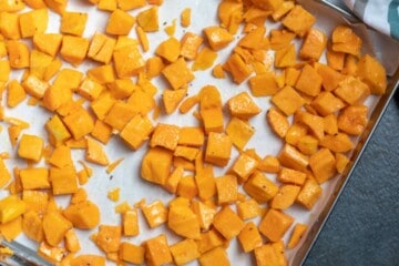 Seasoned butternut squash on roasting pan lined with parchment paper.