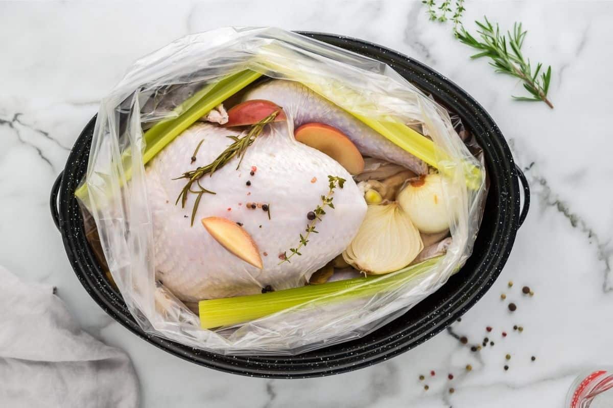 Raw turkey in brine bag along with herbs and onions.