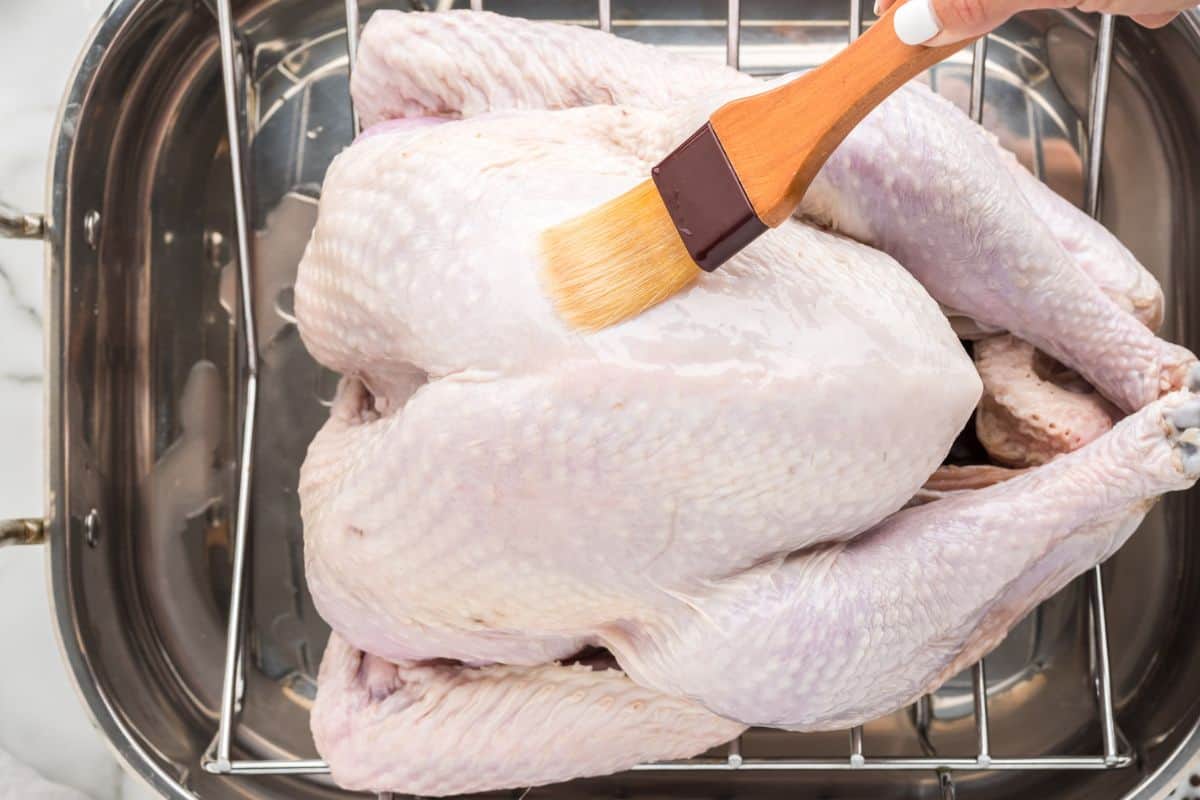 A pastry brush brushing a raw turkey with oil.