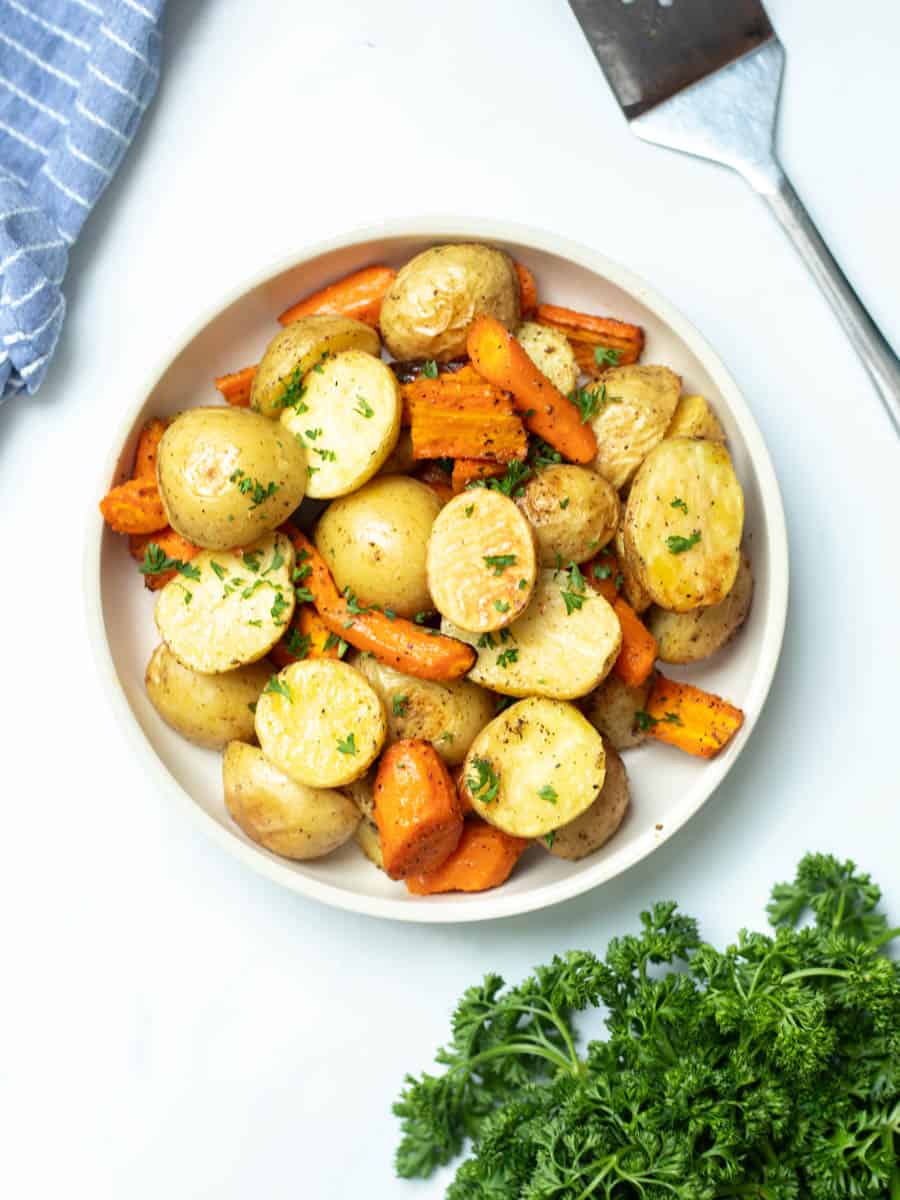 Bowl of roasted potatoes and carrots topped with fresh parsley.