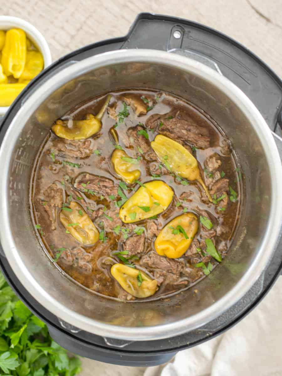Cooked and shredded pot roast in inner pot of Instant Pot topped with Pepperoncini Peppers and parsley.