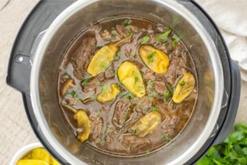 Shredded pot roast inside inner pot with pepperoncini peppers.