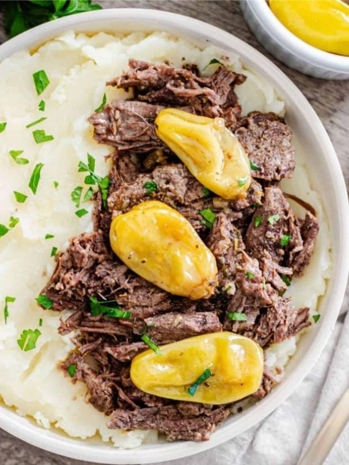 Instant Pot Mississippi Pot Roast dished up with mashed potatoes in serving bowl topped with minced parsley.