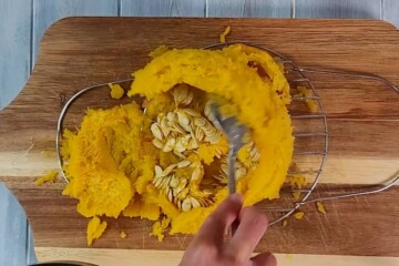 Cooked pie pumpkin on cutting board scooping out seeds.