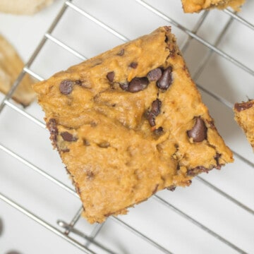 Peanut butter banana chocolate chip bar on cooling rack next to chocolate chips and ripe banana.