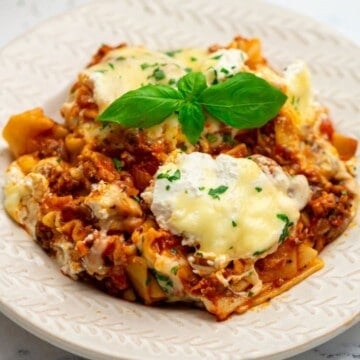 Skillet lasagna served on white plate topped with fresh basil.