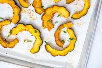 Slices of Roasted acorn squash on parchment paper topped with minced parsley.