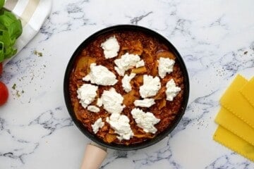 Skillet with cooked beef, spaghetti sauce, and noodles, dolloped with fresh ricotta cheese.