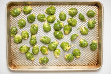 Seasoned halved fresh brussels sprouts on sheet pan spread out.
