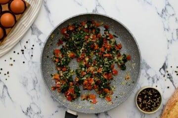 Spinach, roasted red pepper, and onions after being sauteed in saute pan.