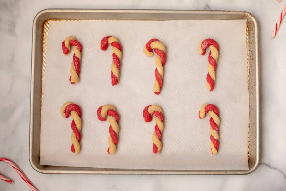 Shaped candy cane cookies on baking sheet topped with sanding sugar.
