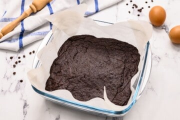 Baked brownies in glass baking dish lined with parchment paper.