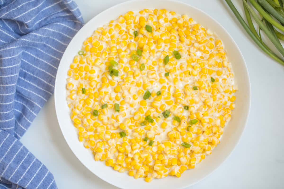 White bowl filled with Instant Pot creamed corn topped with green onions next to blue towel.