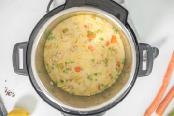 Creamy turkey noodle soup in inner pot of instant pot next to carrots and celery.