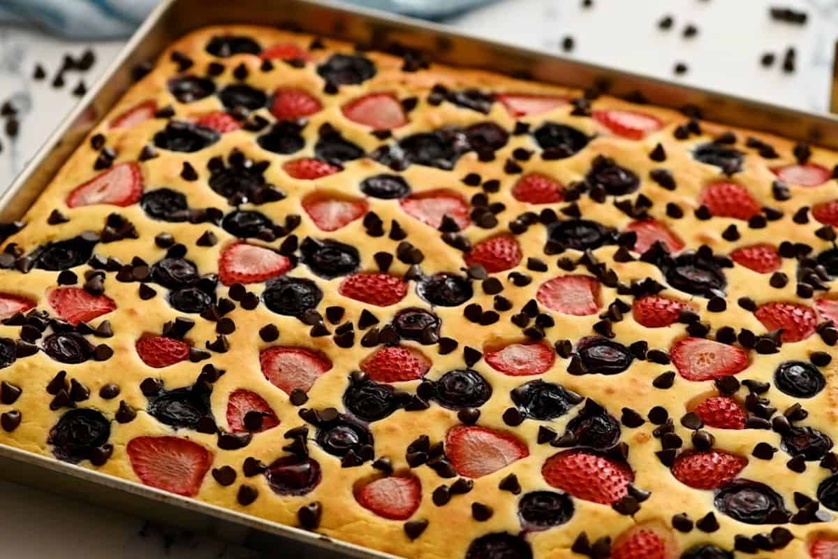 Baked pancake on sheet pan topped with berries and chocolate chips.