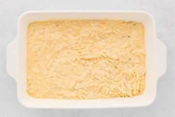 Shredded hashsbrowns with homemade cream sauce spread out in casserole dish.