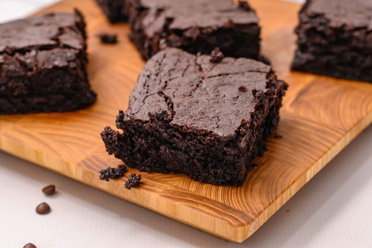 Sliced fudgy brownies on wooden cutting board with chocolate chips scattered around.