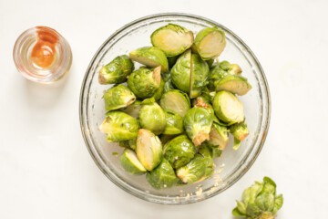 Halved Brussels Sprouts in mixing bowl with garlic, honey, olive oil, and hot sauce.