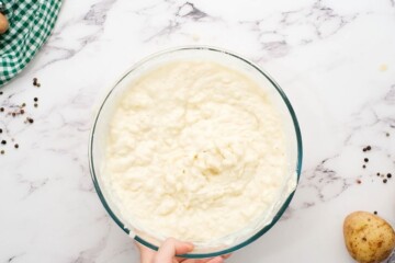 Creamy mashed potatoes, eggs, cream cheese, and onion mixed together in large mixing bowl.