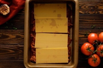 Meat sauce and 4 noodles layered in baking dish for lasagna.