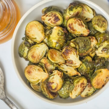 Roasted Brussels sprouts in serving bowl with honey jar in background.