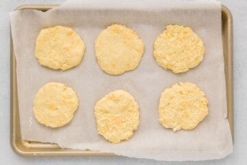 6 shaped mashed potato cakes on parchment lined baking sheet.