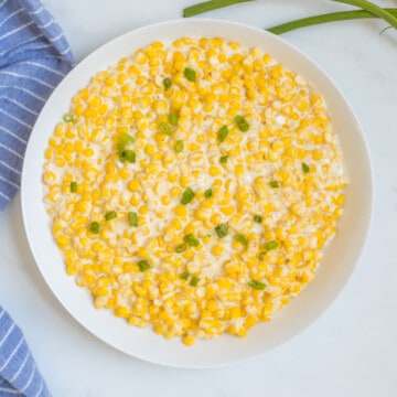White bowl filled with Instant Pot creamed corn topped with green onions next to blue towel.