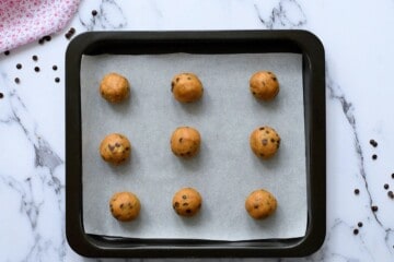 9 rolled cookie dough balls on a parchment lined baking sheet.