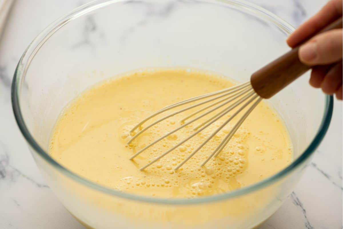Whisk in bowl with eggs, cream, milk, and seasonings whisking together.