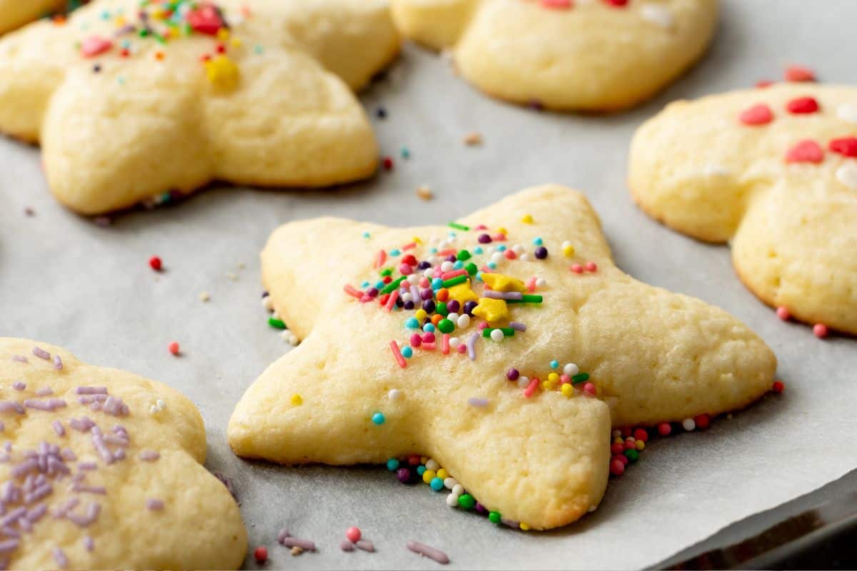 Tray of just baked sugar cookies on baking sheet with sprinkles.