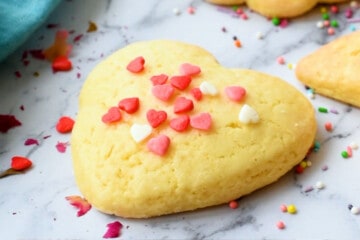 Heart cut out sugar cookie on counter with sprinkles.