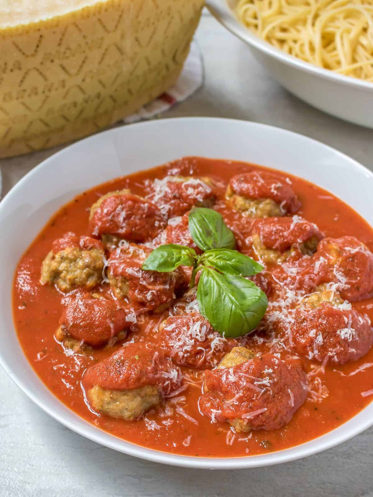 Instant Pot Meatballs in white bowl served with marinara and topped with fresh parmesan and basil.
