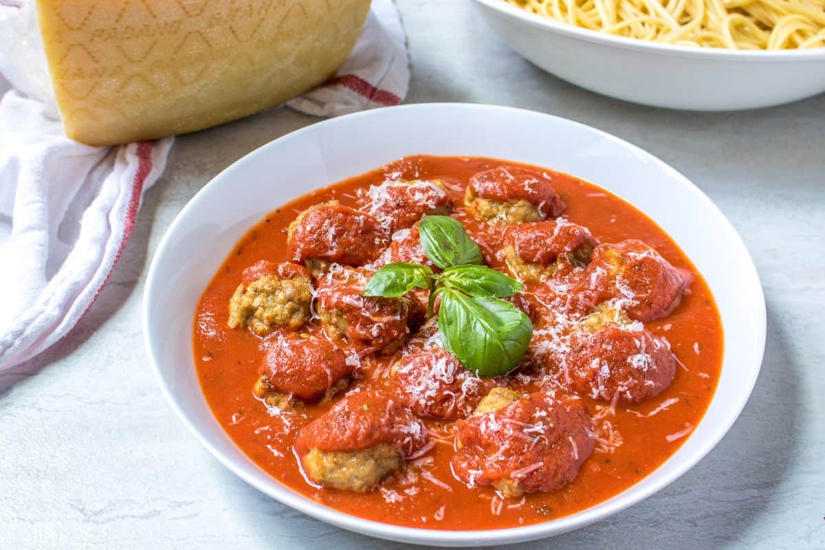 Instant Pot Meatballs in white bowl served with marinara and topped with fresh parmesan and basil.