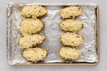8 halves of baked potatoes stuffed with potato filling then topped with shredded white cheddar cheese on sheet pan.