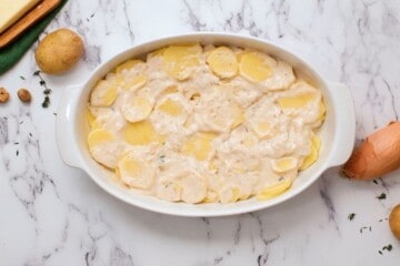 Thinly sliced potatoes with cream sauce in oval white baking dish.