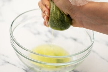 Frozen spinach in cheesecloth being squeezed over large bowl.
