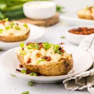 Twice baked potato topped with white cheddar, bacon, and green onions on white plate.