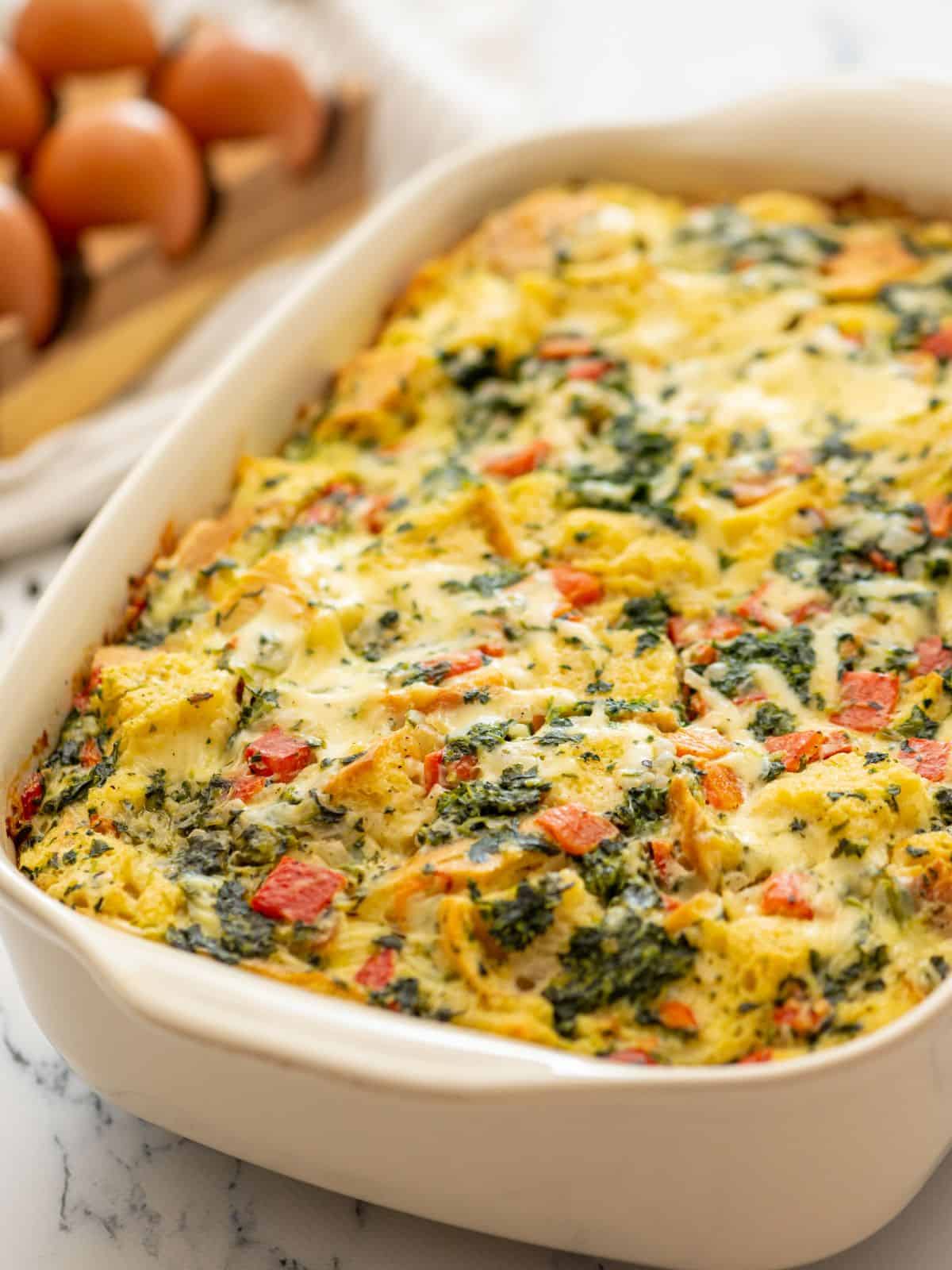 Baked breakfast strata with spinach and red peppers in baking dish.