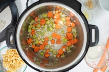 Carrots, onions, celery, and garlic sauteed in pressure cooker with olive oil and butter and ingredients for turkey noodle soup in background.