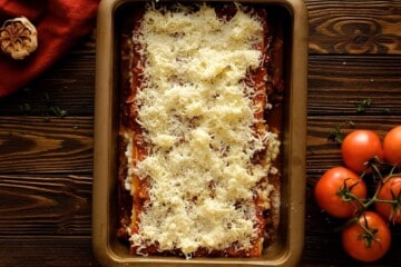 Layered lasagna in 9x13 baking dish next to fresh tomatoes.