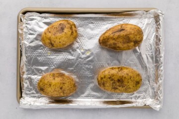 4 russet potatoes on a baking sheet lined with foil.