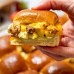Hand holding a breakfast slider made with cheese, sausage, and eggs.