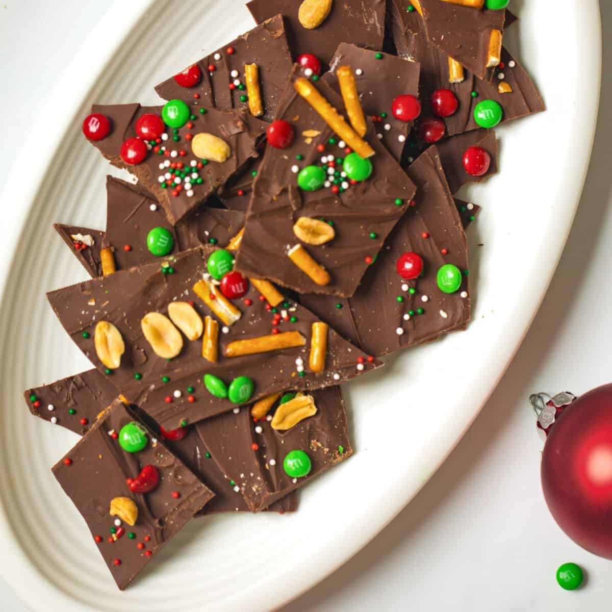 Plate of holiday chocolate bark topped with m&ms, pretzels, nuts, and sprinkles.