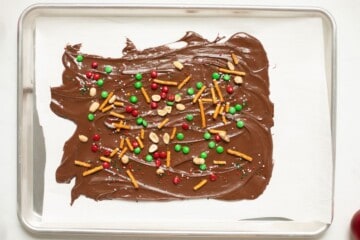 Melted chocolate spread out on parchment paper topped with pretzels, M&Ms, sprinkles and nuts.