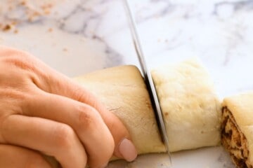 Knife cutting log of cinnamon roll dough into 9 rolls.
