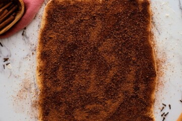 Cinnamon sugar mixture spread over rectangle shaped dough.